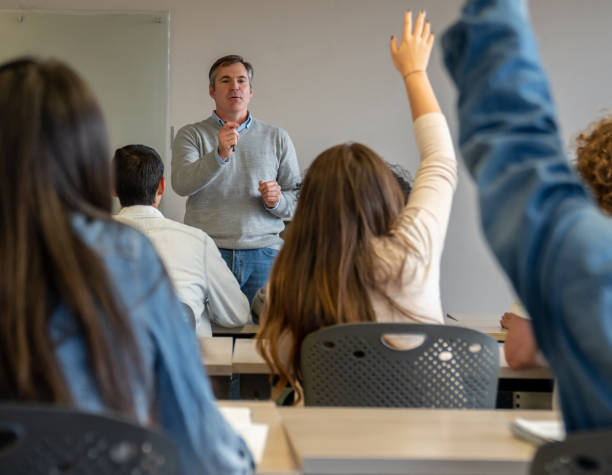 istock Backview of students during class raising hands to answer question to male teacher 1129999773