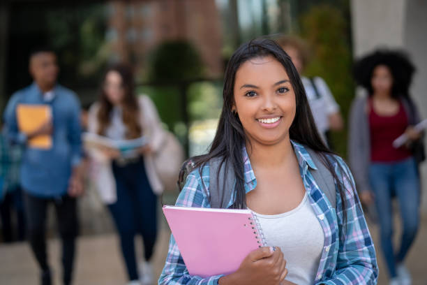 istock Young black pretty female student at college holding her notebooks while facing camera smiling 1129999796