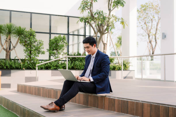istock Happy young businessman using laptop outside office building 1130015413