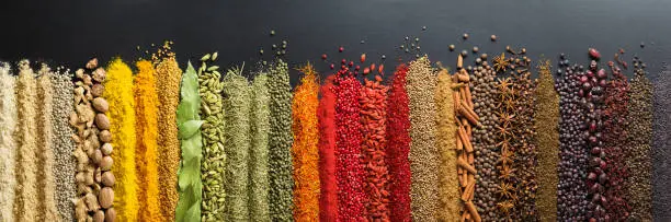 Spices and herbs for website headers. Seasoning scattered on black table, background for packing with food.