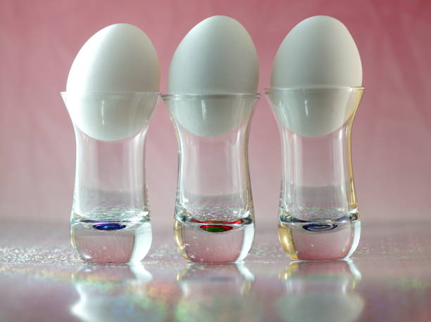 istock Three white eggs in small glasses with mirror reflection on a pink  background abstract conceptual art photography 1130026973