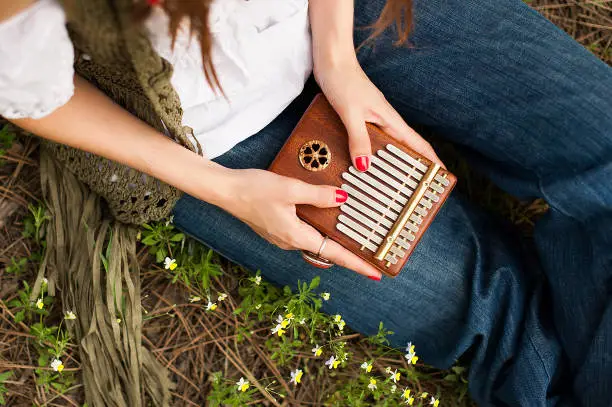 Woman holding kalimba in her hands and playing. Woman sitting on the grass