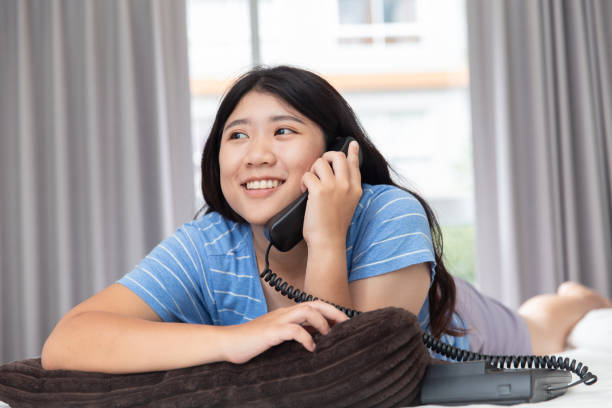 友人と話しての寝室で呼び出し元の固定電話を使用して十代のアジアの女の子 - 加入電話 ストックフォトと画像