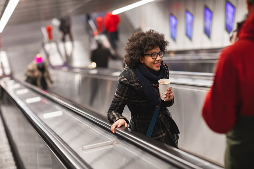 Beautiful young woman drinking coffee on escalator