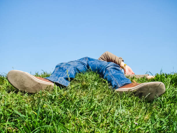 Businessman lays horizontal dreaming in tall green grass under blue sky