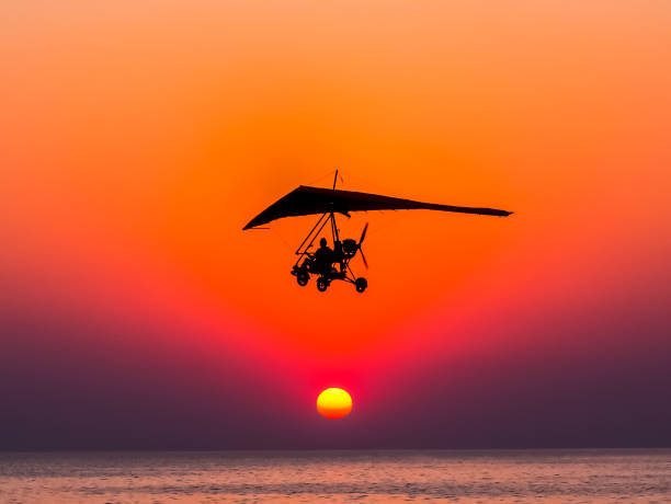 Motorized glider flies against the sunset over the sea. The person flying on a trike with the motor against The hang-glider is flying against the sunset. glider hang glider hanging sky stock pictures, royalty-free photos & images