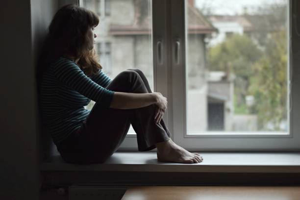 Sad young woman sitting on the window, watching out