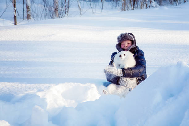 A boy with a white dog Spitz walks in winter in the snow