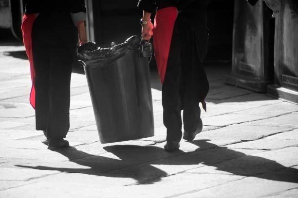 Two restaurant workers with aprons walking, carrying a dust bin in a city street,  taking out the garbage. Santiago de Compostela, Galicia, Spain.