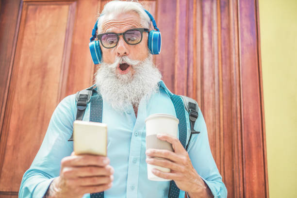 スマート フォンを使用してショックを受けた年配の男性朝時 - 家音楽を聴く、飲むコーヒーから外出しながら技術、トレンディなライフ スタイルとうれしそうな高齢者のライフ スタイルの� - old business men businessman ストックフォトと画像