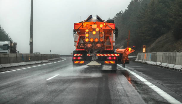 camion de gritter d'entretien d'autoroute orange diffusant le sel de dégivrage, des cristaux tombant sur la route asphaltée recouverte de glace pendant le jour couvert - spreader photos et images de collection
