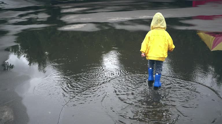 Little boy walking outdoors and jumping on puddle