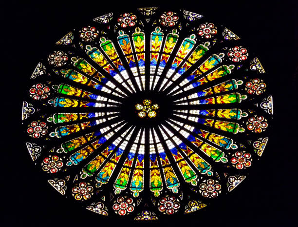 A close up photo of the beautiful, circular stained glass window in the Notre Dame Cathedral found in Strasbourg, France shines its bright colours as the sun lights it up.