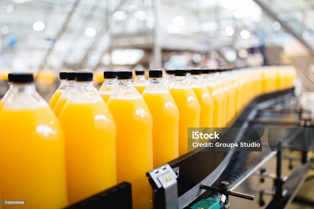 Bottling plant Bottling factory - Orange juice bottling line for processing and bottling juice into bottles. Selective focus. Manufacturing Stock Photo