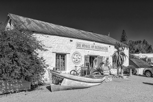 Paternoster, South Africa, August 21, 2018: Die Winkel Op Paternoster, a shop in an historic building in Paternoster on the Atlantic Ocean Coast. A boat and bicycle are visible. Monochrome