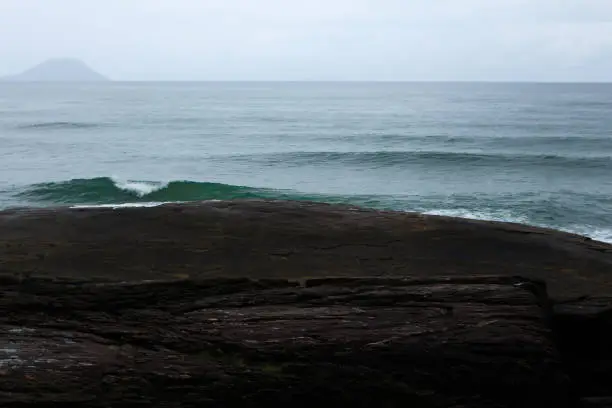tlantic ocean with island in background and waves crashing on black rocks. Bertioga's Beach- Brazil