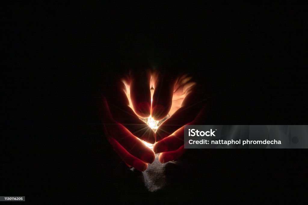 Two hand holding a light bulb in the dark background. Hand Stock Photo