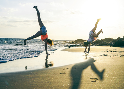 Happy loving family of mother and daughter having fun making acrobatic handstand on the beach at sunset - Young mom enjoying time with her kid  playing together outdoor - Family lifestyle concept