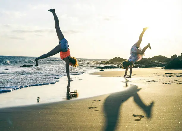 Photo of Happy loving family of mother and daughter having fun making acrobatic handstand on the beach at sunset - Young mom enjoying time with her kid  playing together outdoor - Family lifestyle concept
