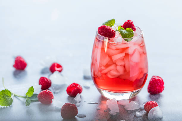 Refreshing red drink with fresh raspberries and crushed ice A refreshing red translucent raspberry drink with ice and fresh raspberries. The juice is garnished with a green leaf, and there are pieces of ice and raspberries scattered around the drink. saint vincent and the grenadines stock pictures, royalty-free photos & images