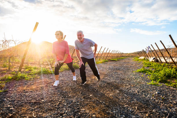 couple de senior adulte faire activité sportive le matin pour rester en bonne santé et longue durée de vie ensemble - remise en forme et étirements pour société de personnes âgée - personnes faisant concept outdoor activités de remise en forme - morning italy shadow sunlight photos et images de collection