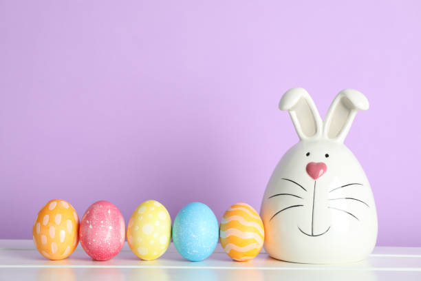 istock Decorated bunny and Easter eggs on table against color background. Space for text 1130125279