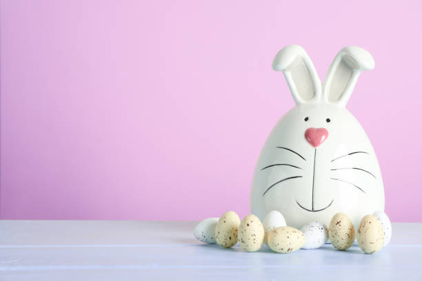 istock Decorated bunny and Easter eggs on table against color background. Space for text 1130125346