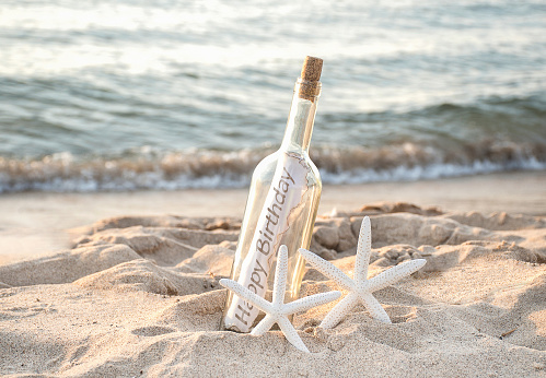 pair of white starfish with happy birthday message in a bottle on beach sand