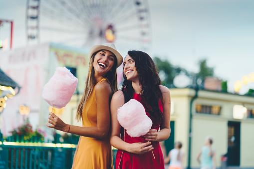 Young women eating pink cotton candy and having fun at the amusement park