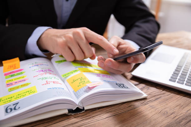istock Businessman Holding Cellphone Writing Schedule In Diary With Pen 1130134966