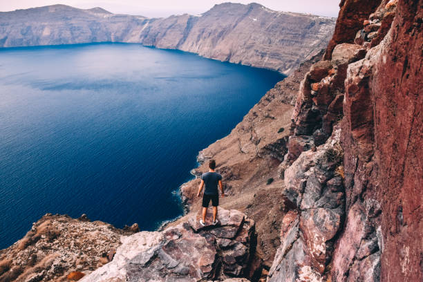 istock Rear View of Man Standing on Cliff Overlooking Sea, Greece 1130136543