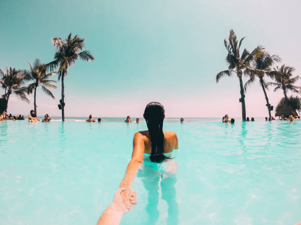 Girlfriend Pulling Boyfriend By Hand in Swimming Pool on Tropical Vacations.