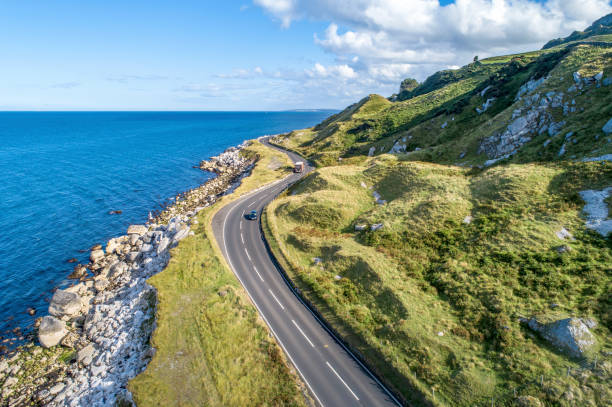 Causeway Costal Route in Northern Ireland, UK Causeway Costal Route with cars, a.k.a. Antrim Coastal Road on eastern coast of Northern Ireland, UK. coastal feature stock pictures, royalty-free photos & images