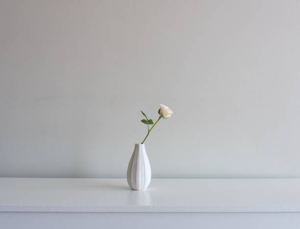 istock Single pale pink rose on small vase on white table 1130153458