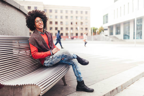 istock A handsome young Egyptian curly guy sitting on a bench dressed in a bright orange sweater and jeans. Happy people. The student walks in the break between the lessons. 1130153595