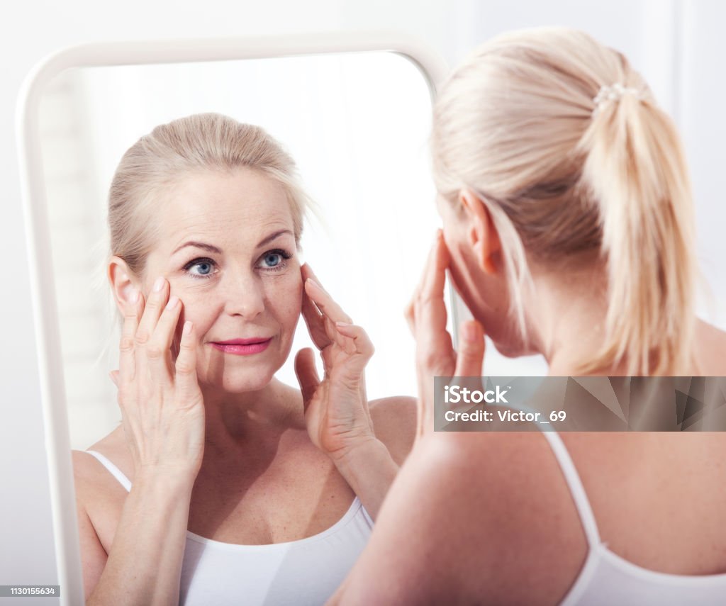 Femme regardant les rides en miroir d’âge moyen. Chirurgie plastique et injections de collagène. Maquillage. Visage de macro. Mise au point sélective - Photo de Miroir libre de droits