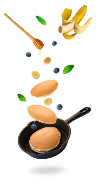 Homemade pancakes, blueberries and banana flying into iron skillet isolated on white background.