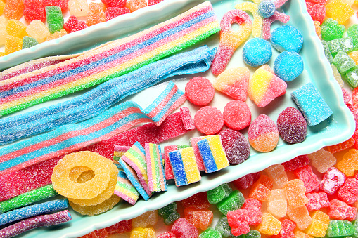 Assorted variety of sour candies includes extreme sour soft fruit chews, keys, tart candy belts and straws. Flat lay, sugar background concept for kids birthday party.