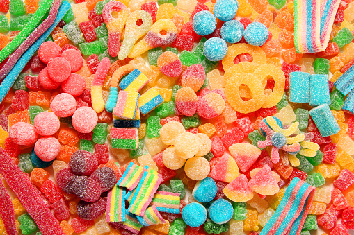 Assorted variety of sour candies includes extreme sour soft fruit chews, keys, tart candy belts and straws. Flat lay, sugar background concept for kids birthday party.