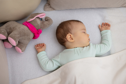 Adorable baby sleeping at night. Little girl in pajama taking a nap in room with toy.