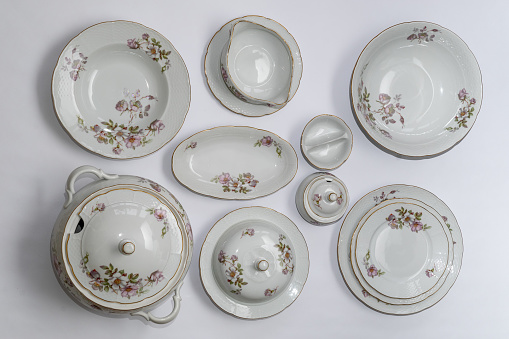 Set of vintage ceramic factorycrafted tableware with flowers of subtle colors on white tablecloth, 11 pieces, top view