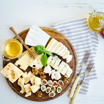 Cheese platter: Parmesan, cheddar, gouda, gorgonzola, brie and other with walnuts, olive oil and honey on wooden board on white background. Tasty appetizers with different kind of cheese. Top view.