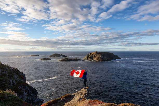 Woman by the ocean cliff Adventurous woman holding a Canadian Flag on a Rocky Atlantic Ocean Coast during a sunny day. Taken in Sleepy Cove, Crow Head, Twillingate, Newfoundland, Canada. newfoundland and labrador photos stock pictures, royalty-free photos & images