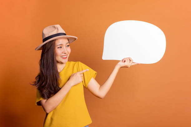 istock Young Asian woman show text box, speech bubble and copy space over orange background, empty space for text and ads, studio light 1130199447