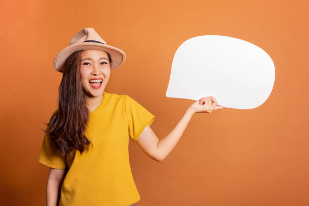 istock Young Asian woman show text box, speech bubble and copy space over orange background, empty space for text and ads, studio light 1130199452