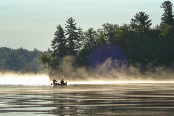 Two men canoeing at dawn on a misty morning. Lake Kashwakamak, North Frontenac, Ontario, Canada