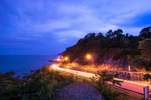 istock twilight light tail on smooth curve road beside the ocean - can use to display or montage on product 1130207675