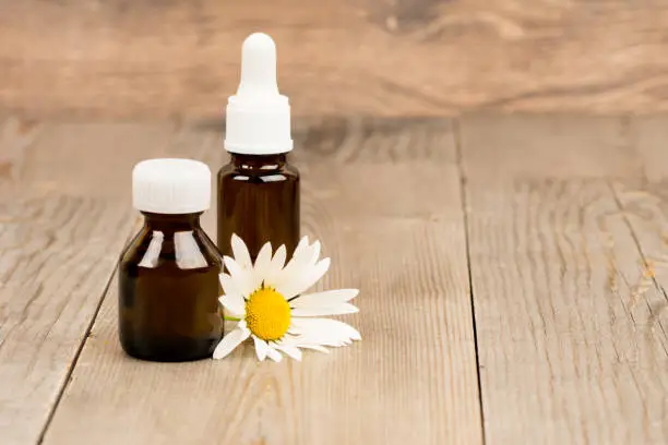 chamomile flowers and essential oil in brown glass bottles on wooden rustic table