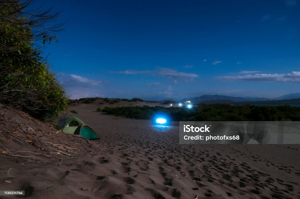 Camping In the Bani  Dunes at Night Descriptive scene of the night sky with the Milky Way during the eclipse of the moon on January 21, 2019, where the Orion, Pleiades, Can Major and thousands of stars in very dark skies are clearly seen on the sand dunes of Bani in the Dominican Republic. A blue tent enhances the interest of the composition where all the elements draw attention to venturing into adventure tourism Adventure Stock Photo