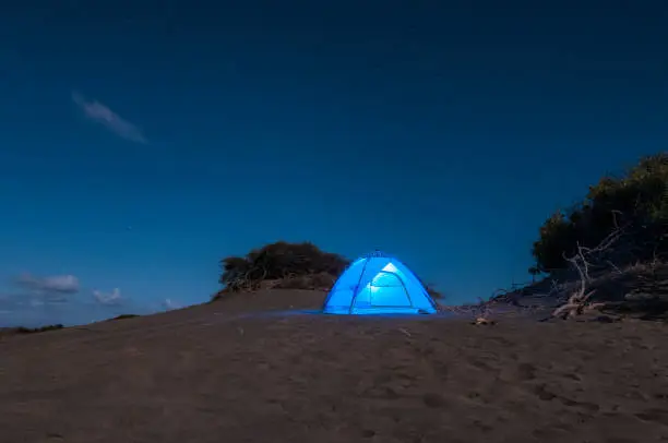 Descriptive scene of the night sky with the Milky Way during the eclipse of the moon on January 21, 2019, where the Orion, Pleiades, Can Major and thousands of stars in very dark skies are clearly seen on the sand dunes of Bani in the Dominican Republic. A blue tent enhances the interest of the composition where all the elements draw attention to venturing into adventure tourism